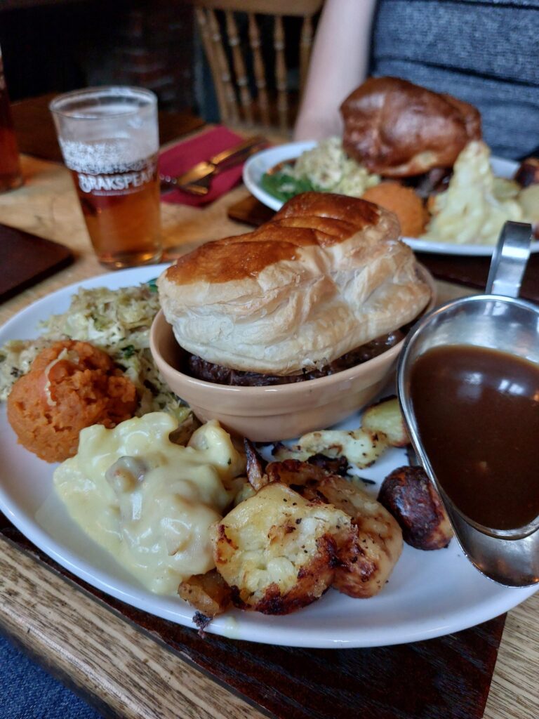 A large plate of food, with a puff pastry pie surrounded by a variety of vegetable sides