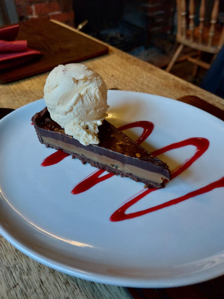A slice of chocolate tart, with a scoop of ice cream and red drizzled sauce
